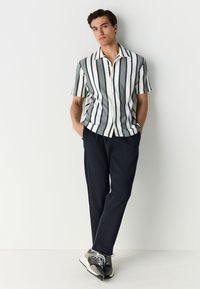 Korte mouwen overhemd met verticale strepen in marineblauw en wit, gecombineerd met donkerblauwe broek en grijze sneakers. Platte kraag ontwerp.