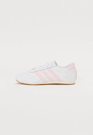 Baskets basses blanches avec trois bandes roses, lacets blancs et semelle en gomme, vues de profil sur un fond blanc.