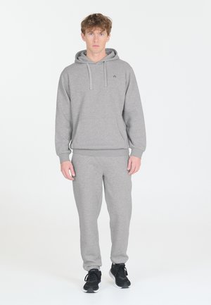Grå hoodie og bukser sæt lavet af blødt materiale. Har en frontlomme og snore. Sammen med sorte sportssko.