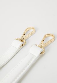 Weiße Lederband mit Clips aus goldfarbenem Metall, mit eingravierter Markenbezeichnung und glatter Oberfläche. Zwei Clips, die mit runden Ringen verbunden sind.