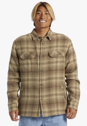 Chemise en flanelle à carreaux bruns et beiges avec un devant à boutons, deux poches poitrine et une coupe décontractée. Texture douce et manches longues.