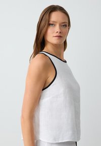 Débardeur en lin blanc avec finitions noires, avec une coupe décontractée et sans manches. Texture lisse avec un ourlet arrondi.
