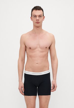 Sorte boxertruser med en hvit elastisk midjebånd merket "COPENHAGEN STUDIOS," tettsittende design, glatt tekstur og midt-til-lår lengde.