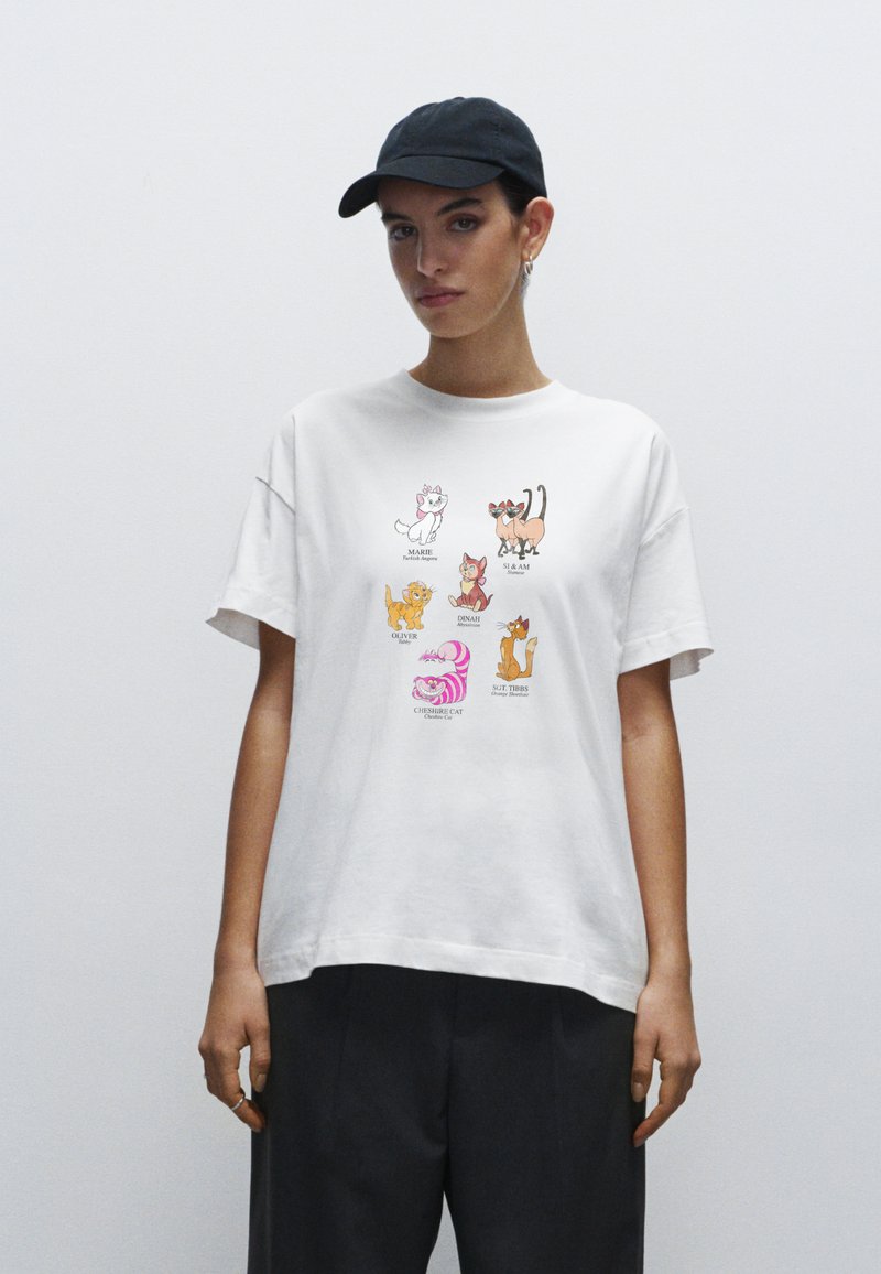 Hvid bomulds t-shirt med cartoon-katte i forskellige positioner og farver, med en afslappet pasform og korte ærmer. Sæt sammen med mørke bukser.