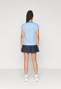 Ριγέ μπλε και λευκό πόλο μπλουζάκι με κοντά μανίκια, συνδυασμένο με ναυτική πλισέ φούστα, φορεμένο με λευκά αθλητικά παπούτσια και κάλτσες μέχρι τον αστράγαλο.