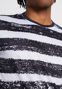 Černobílé pruhované tričko s texturovaným potiskem. Krátké rukávy a kulatý výstřih s kontrastním tmavým obšitím.