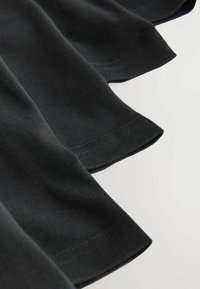 Gros plan sur un tissu noir avec des ourlets cousus visibles et des plis doux sur un fond clair.