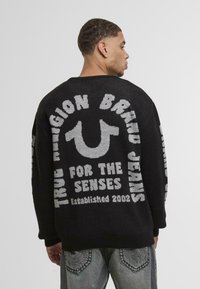 Black knitted sweater featuring gray text and a logo design on the back, with a relaxed fit and long sleeves.