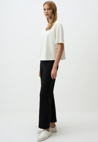 T-shirt bianco a maniche corte abbinato a pantaloni neri aderenti e sneakers bianche. L'outfit presenta una silhouette rilassata e texture di tessuto lisce.