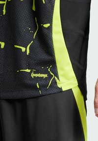 Schwarzes Sportshirt mit neon-gelben Akzenten und Spritzdesign. Es besteht aus atmungsaktivem Mesh-Stoff und hat ein Logo-Tag am Saum.