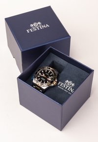 Montre Festina dans une boîte navy. Comprend un cadran noir, une lunette dorée avec des chiffres, des accents en acier inoxydable et un intérieur texturé bleu.
