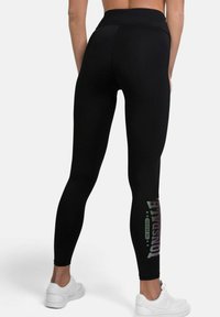 Black leggings with a high waistband, featuring a shiny logo design in gradient colors along the left leg and a smooth, stretchy fabric.