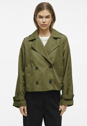 Olive green cropped jacket with double-breasted buttons, wide lapels, and additional fabric accents at the cuffs. Smooth, slightly shiny fabric.