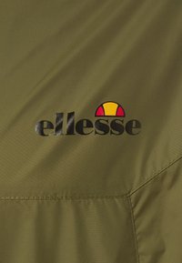 Tessuto verde oliva con il logo nero "ellesse" e un design semicircolare colorato in rosso, giallo e nero. Texture liscia con dettagli di cucitura.