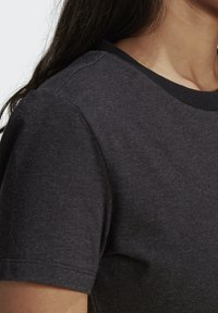 Svart bomullströja med rundad halsringning, korta ärmar och en mjuk textur, som visar detaljer av axelsöm och halsringning.