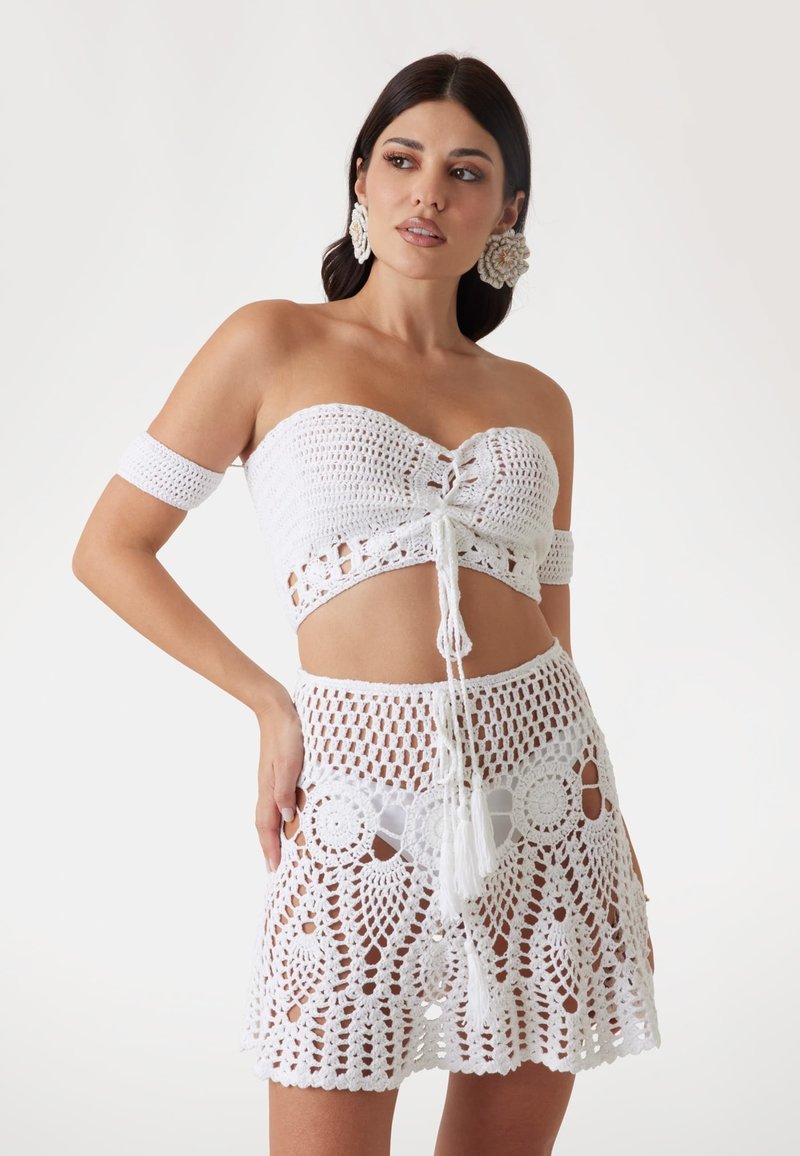 Witte gehaakte twee-delige set met een strapless top met strikdetails en een hoog-getailleerde rok met cirkelvormige uitsparingen en franjes.