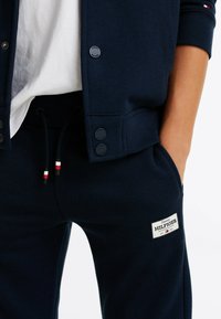 Granatowy sweter z guziczkami i ściągaczami, w połączeniu z granatowymi dresami z białą łatą z logo oraz sznurkiem w czerwono-białe akcenty.