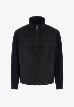 Schwarze Jacke mit Reißverschluss vorne, kuscheligem Kragen und strukturierten Strickärmeln. Weiches Innenmaterial mit seitlichen Taschen und tailliertem Schnitt.