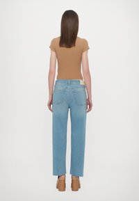 Světle modré džíny ze džínoviny se střihem na rovno, vysokým pasem a třepenými lemy, doplněné o přiléhavý hnědý žebrovaný top a tělové platformové podpatky.