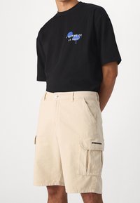 Černé bavlněné tričko s modrým textovým motivem, spárované s béžovými cargo šortkami s bočními kapsami a logem na noze.