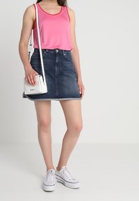 Rosa ärmlös topp med röd kant, denim mini-jurk, vit axelväska och vita sneakers. Slät tyg och klassisk denimstruktur.