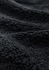 Tissu noir texturé avec une surface douce rappelant la polaire, présentant des fils bouclés et surélevés. Le matériau présente une teinte riche et foncée.