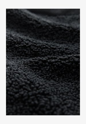 Czarna, teksturowana tkanina o miękkiej, przypominającej fleecę powierzchni z wypukłymi, pętlami nici. Materiał ma intensywny, ciemny odcień.
