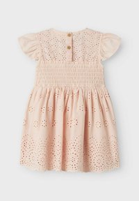 Robe rose pâle avec des manches courtes en volants, corsage smocké et détails en broderie anglaise complexes au niveau de la jupe et de l'ourlet. Fermeture à deux boutons en bois au dos.