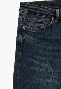 Jeans de mezclilla azul oscuro con una textura suave, diseño de cinco bolsillos y detalles de costura naranja a lo largo de las costuras y bolsillos.