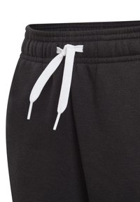 Pantalones de chándal negros con un tejido texturizado, que cuentan con una cintura elástica y una cuerda blanca. La vista en primer plano resalta el detalle del nudo.