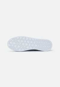 Semelle de basket blanche présentant un motif de semelle géométrique avec des accents surélevés. Bords lisses et zone de orteil légèrement surélevée.