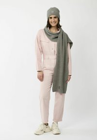 Roze overall met een knoopsluiting aan de voorkant, gecombineerd met een grijze geribbelde sjaal en bijpassende muts. Bevat een logo patch op de muts. Crème sneakers.