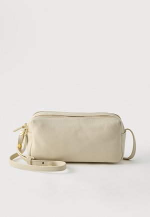 Pochette rectangulaire en cuir couleur crème avec fermeture éclair dorée et sangle ajustable sur fond blanc.