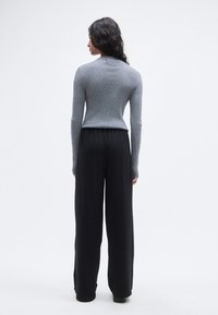 Γκρίζο μακρυμάνικο τοπ με ριμπ υφή, συνδυασμένο με μαύρο, χαλαρά εφαρμοστό παντελόνι, που αναδεικνύει μια άνετη εφαρμογή και απαλή υφή. Το σύνολο είναι μινιμαλιστικό.