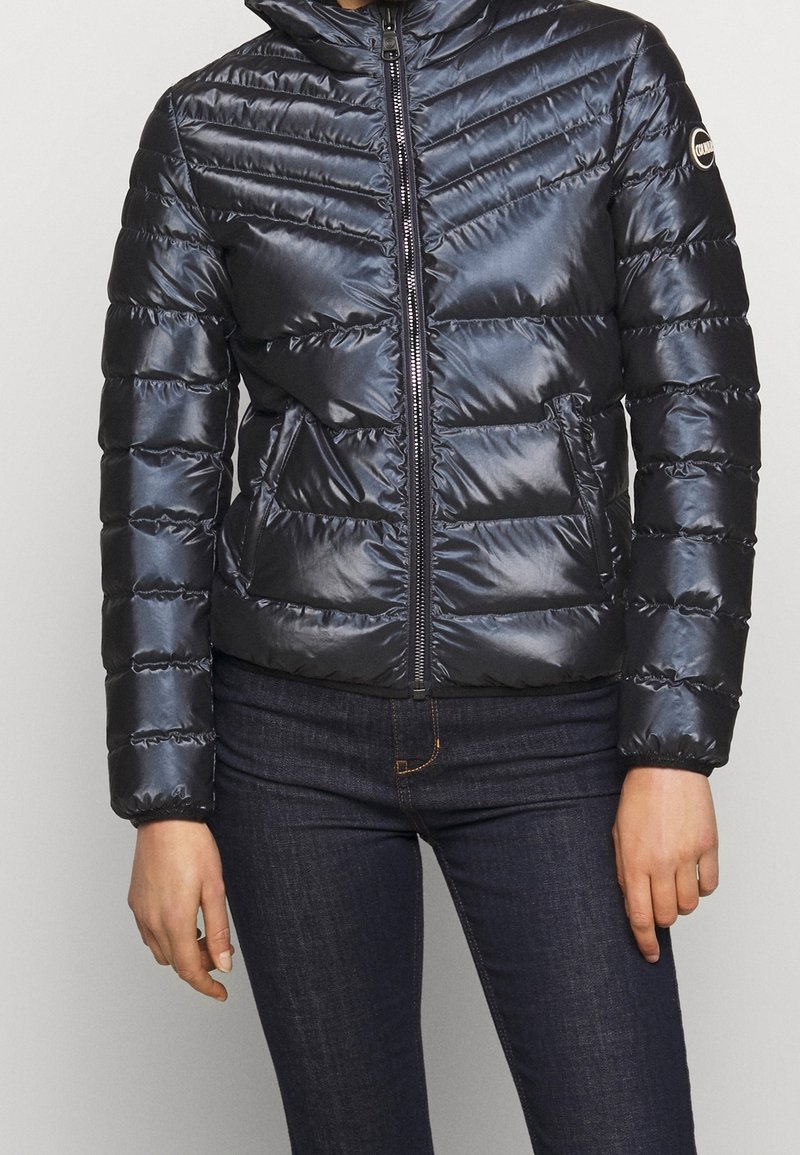 Laivaston sininen toppatakki, jossa siksak-mallinen tikkaus, korkea kaulus ja vetoketju edessä. Takissa on sileä, kiiltävä pinta ja sivutaskut.