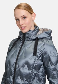 Grijs gewatteerd jack met een glanzende afwerking, hoge kraag, verstelbare capuchon en zwarte banden; heeft een geometrisch patroon op de stof.