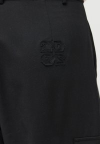 Tissu noir avec texte brodé en noir en relief indiquant "2ND CNR" sur la partie haute avant d'un vêtement.