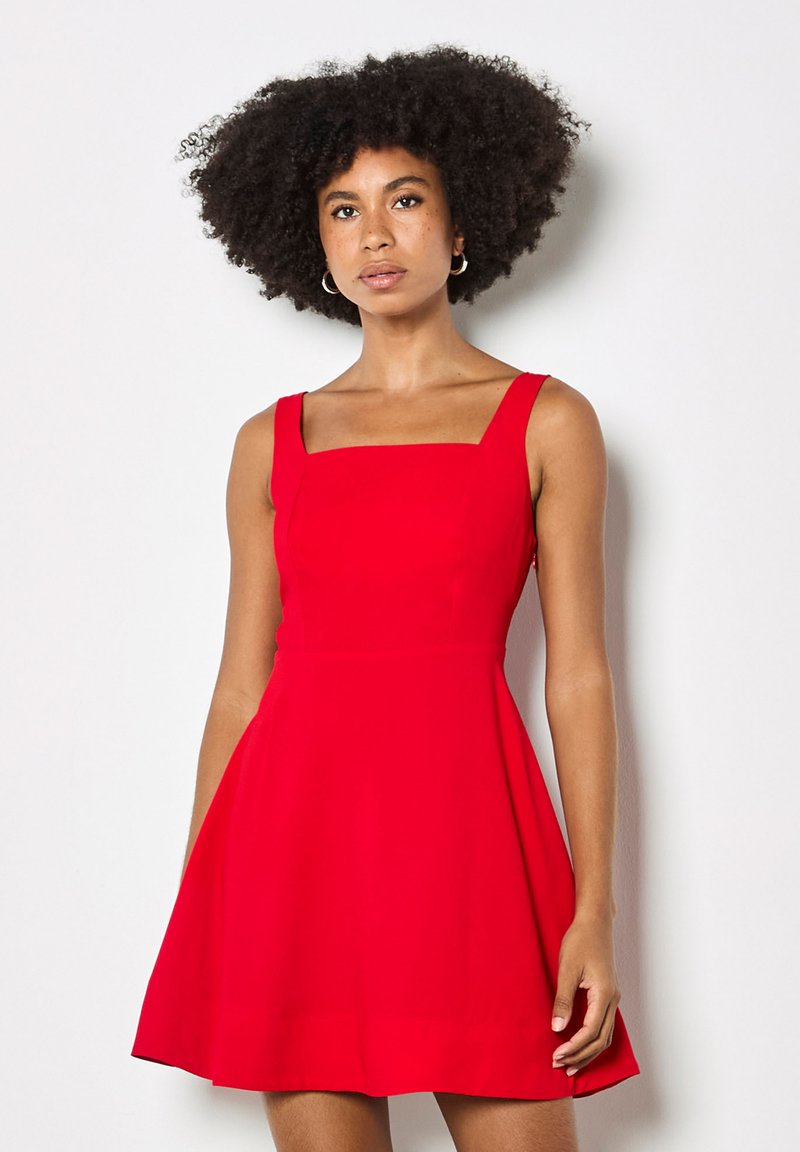 Robe rouge sans manches avec un décolleté carré, un corsage ajusté et une jupe évasée, en tissu lisse. Design minimaliste sans motifs ni accents.