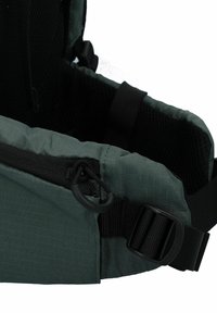 Donkergroene stoffen drager met een gewatteerd ontwerp, mesh achterkant, verstelbare banden en een ritsvak met zwarte sluiting en lus hardware.