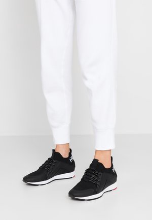 Czarne buty sportowe z teksturowaną siateczkową cholewką, kontrastową białą podeszwą i sznurowadłami. Na boku znajduje się logo białymi literami.