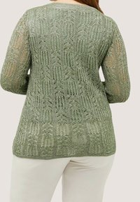 Pull en maille verte avec un motif en maille ouverte, manches longues et encolure arrondie, présentant un motif texturé de feuilles.