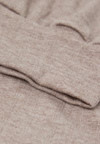 Hellbrauner Strickstoff mit weicher Textur, der eine gefaltete Kante aufweist und subtile Farbvariationen im gesamten Material zeigt.