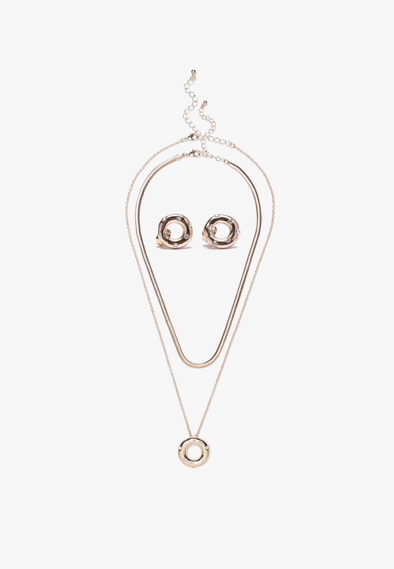 Collana dorata con doppie catene e pendente a cerchio; orecchini circolari abbinati con cristalli; texture liscia e design moderno.
