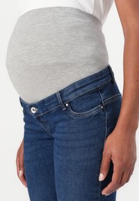 Ceinture de soutien pour le ventre en jersey gris sur un jean bleu foncé, mettant en valeur un ajustement serré. La ceinture est douce, tandis que le jean présente un style classique à cinq poches.