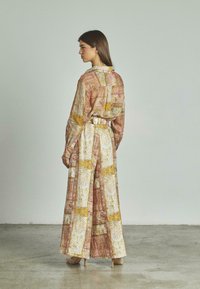 Vestido largo y fluido de satén estampado en tonos de rosa, dorado y blanco. Presenta un collar con botones y un detalle de cintura ajustada con cinturón.