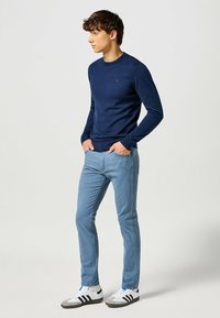 Suéter de punto navy con cuello redondo, combinado con jeans ajustados de color azul claro y zapatillas blancas con rayas negras. El modelo está de lado.