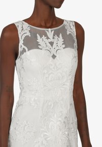 Weißes Kleid mit transparenter bestickter Borte, die aufwendige florale Muster zeigt, und einer schmalen Silhouette. Weicher Stoff und elegantes Design.
