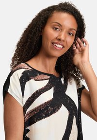 Lightweight top featuring a cream background with abstract black and copper patterns, short sleeves, and a rounded neckline.