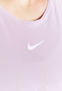 Maglietta atletica di un leggero viola con scollatura rotonda, tessuto testurizzato e logo Nike a forma di swoosh bianco sul davanti.