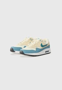 Hellbeige Sneakers mit einem blauen Swoosh, ausgestattet mit einem geschichteten Design und strukturiertem Material. Gummisohle mit sichtbarer Luftpolsterung.